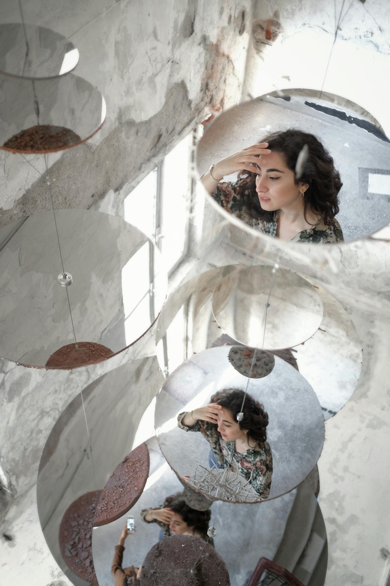 Suspended circular mirrors reflecting a figure from many angles
